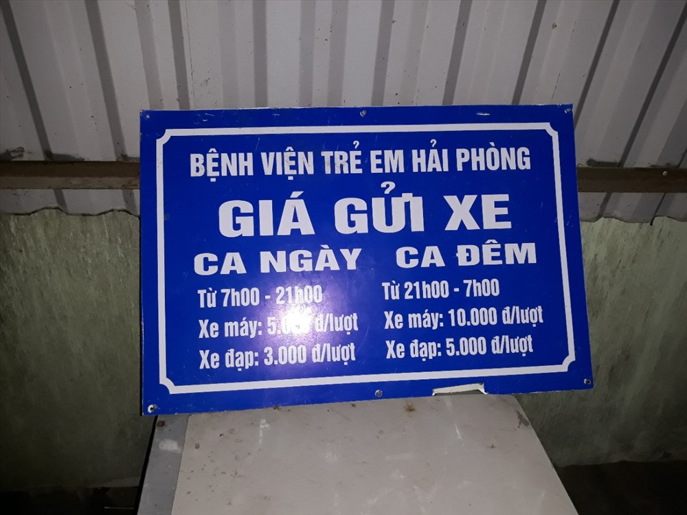 Nhân viên nhà xe bệnh viện trẻ em Hải Phòng cho biết tấm biển này là quy định thu phí gửi xe - Ảnh TN