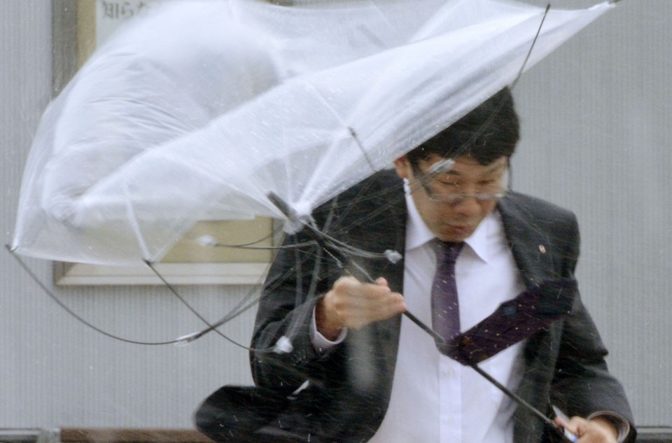 Một người đàn ông Nhật Bản đang chật vật trên đường vì gió mạnh. Ảnh: Kyodo