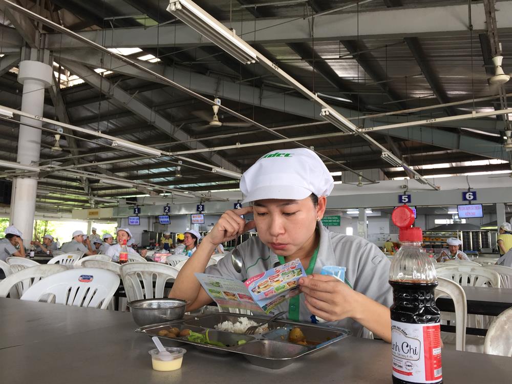 Nữ công nhân ăn trưa, tranh thủ tìm hiểu thông tin sản phẩm của House Foods Việt Nam - Ảnh: L.T