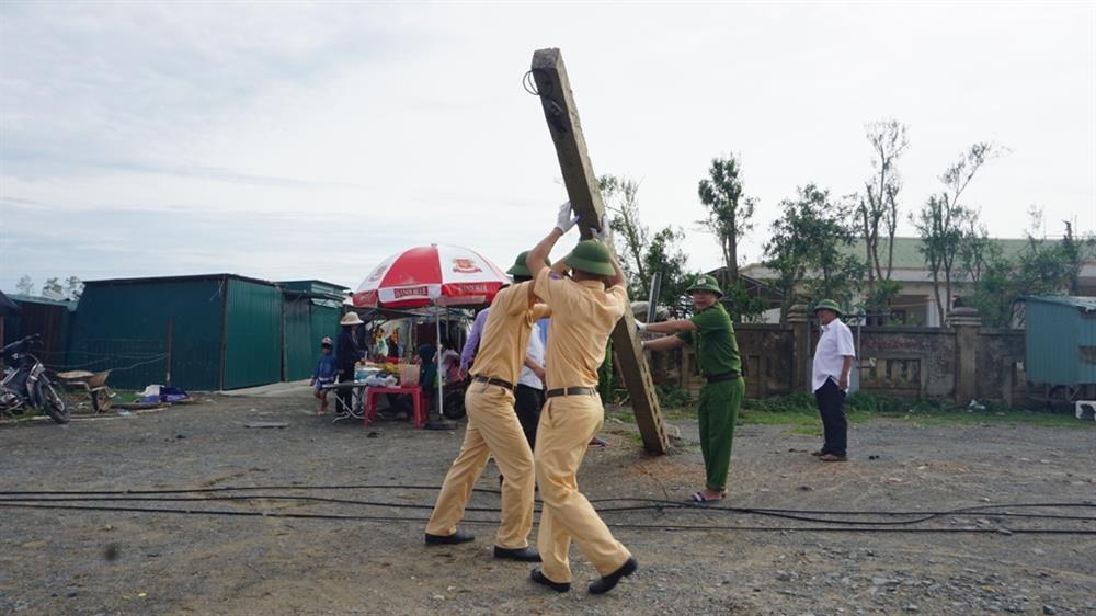 Các sĩ quan CSGT giúp dân dựng lại cột điện ngã. Ảnh: QĐ