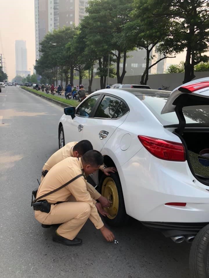 Hai chiến sĩ Cảnh sát giao thông - Công an Hà Nội giúp người phụ nữ thay lốp xe hỏng. Ảnh: Nguyễn Hương