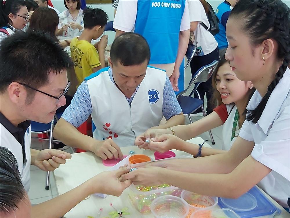 Học sinh Trường Chuyên biệt Bình Tân (phải) hướng dẫn thành viên Cty PouYuen Việt Nam làm vòng cườm thủ công. Ảnh Nam Dương