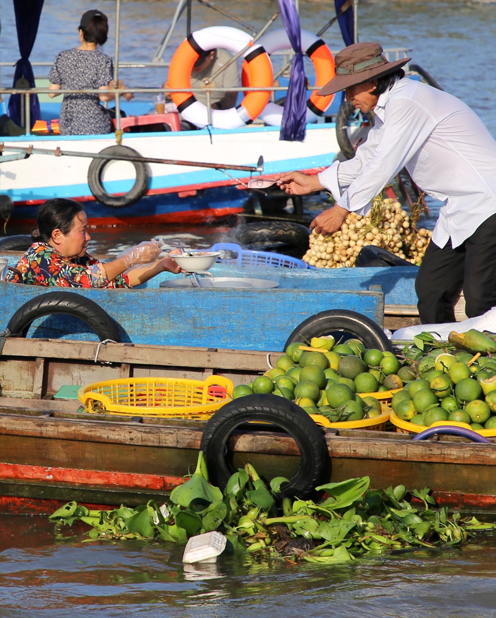 Ngay trên ghe, người dân bán đủ các loại trái cây, thậm chí là thức ăn như bún, hủ tiếu. Tuy nhiên, nhiều loại rác bị vứt thẳng xuống sông. Trong ảnh, dưới khóm lục bình có nhiều loại rác vướng lại.