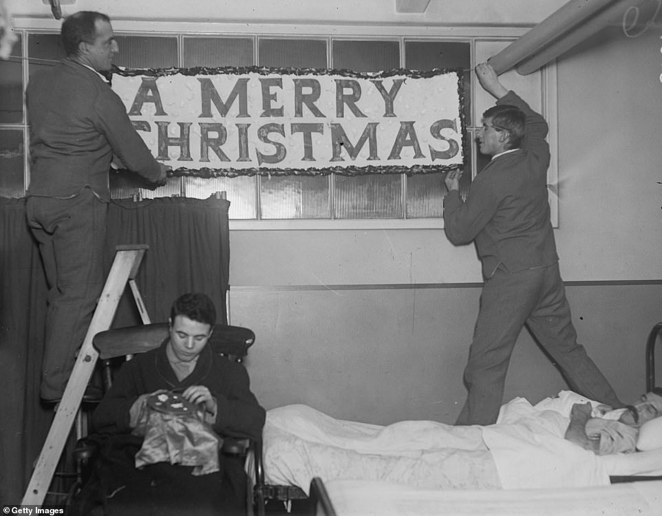 Năm 1916, hai nam giới đang đứng trên giường để treo dòng chữ “Giáng sinh vui vẻ” tại Bệnh viện Quân đội King George.