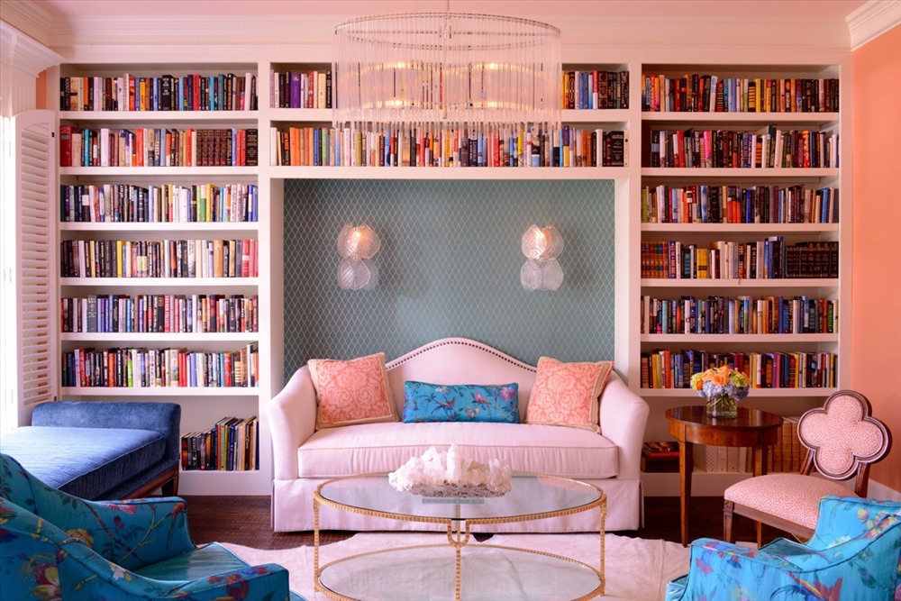 Một phòng khách chủ đạo là màu hồng phấn, được tô điểm bởi hai chiếc ghế sofa xanh biển tươi tắn và rất nhiều sách xếp ngay ngắn trên kệ.