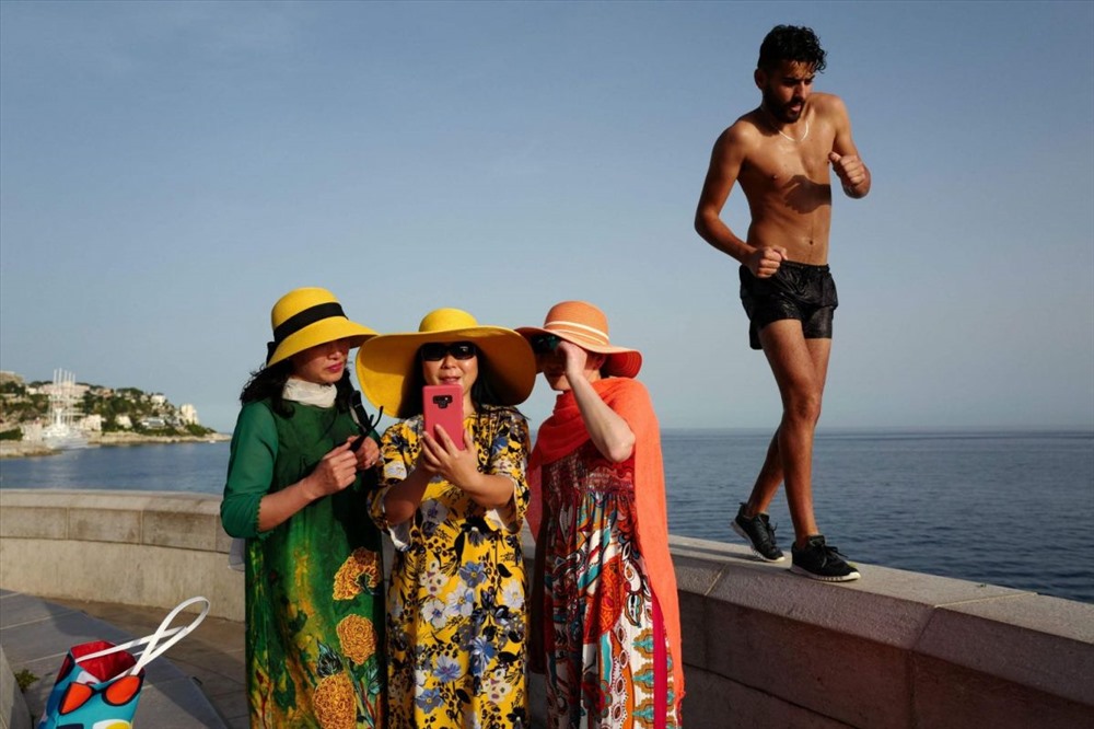 Một người đàn ông đi bộ qua khi du khách đang selfies bên bờ biển French Riviera thuộc thành phố Nice, Pháp. Ảnh: AFP.