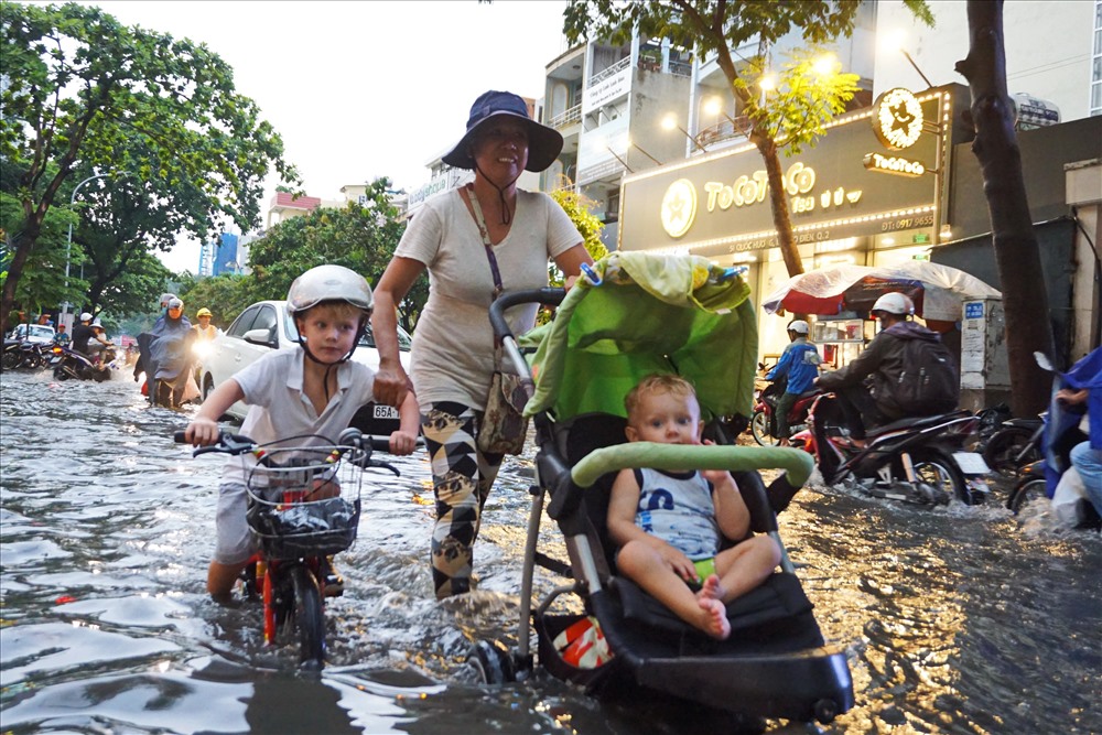 Một người phụ nữ dò từng bước đi, đẩy xe nôi trẻ em trên đường ngập nước.