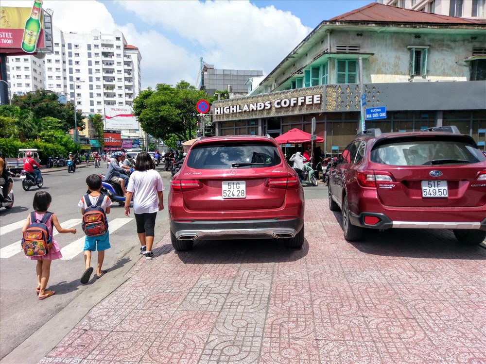 Hai chiếc xe ô tô đậu trên vỉa hè đường Lê Lai (Q.1) khiến các em nhỏ phải đi bộ dưới lòng đường nguy hiểm. Ảnh: M.Q