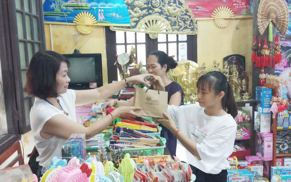 Du khách được nhân viên quầy hàng lưu niệm ở nhà Hữu Vu tặng túi xách giấy, thân thiện với môi trường.