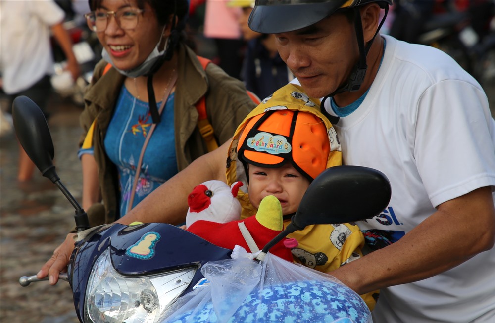 Trẻ khóc thét trên môtô khi di chuyển trên đường ngập nước. Ảnh: Hưng Thơ.