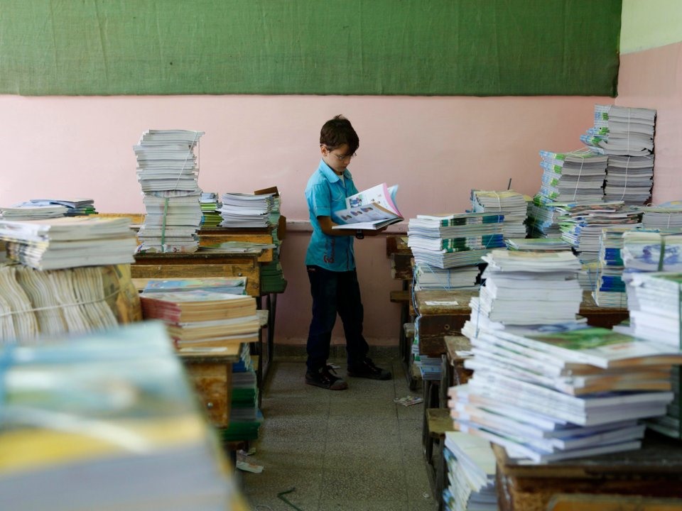 Một bé trai Syria xem xét một cuốn sách vào ngày đầu tiên trở lại trường học ở ngoại ô Damascus. Ảnh: Reuters.