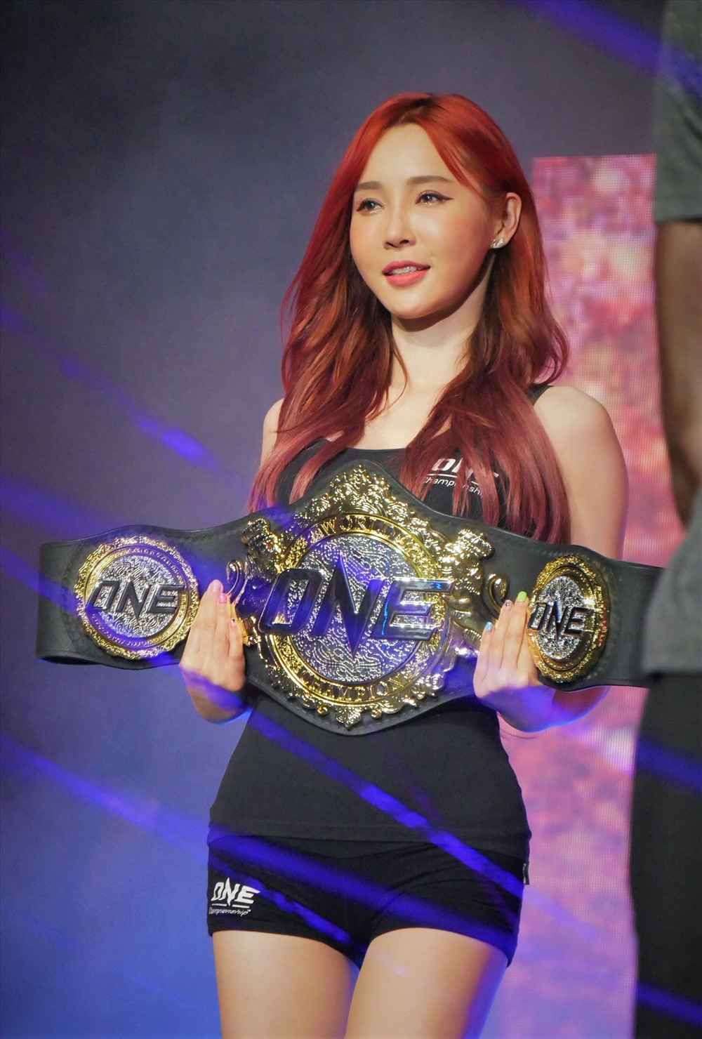 Xuất hiện sớm nhất tại sự kiện, “Ring Girls” Lee Jina với màu tóc đỏ nổi bật, khoe dáng bên cạnh chiếc đai vô địch được đúc bằng vàng và bạc nguyên khối, với trọng lượng gần 15kg, trị giá tới 5 tỷ đồng. Ảnh: Anh Tú