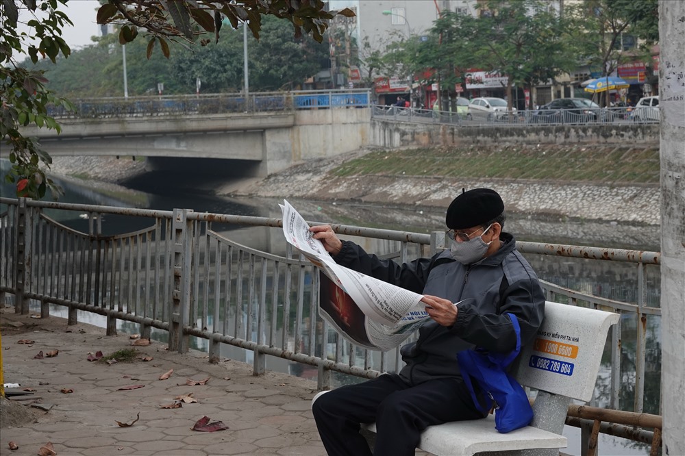 Ông Phạm Phi Hồng, nhà sát sông Tô đoạn chảy qua phường Kim Giang, phải đeo khẩu trang khi ngồi đọc báo.