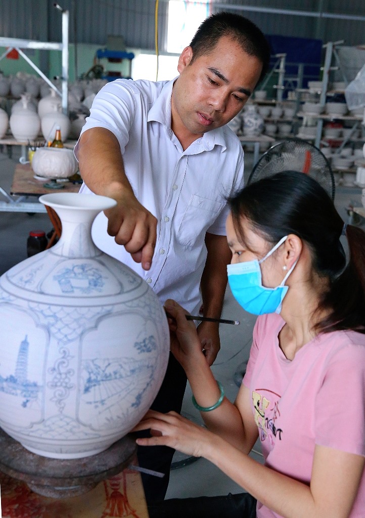 Anh Phạm Văn Vang, hướng dẫn công nhân tạo họa tiết trên những sản phẩm gốm. Ảnh: NT