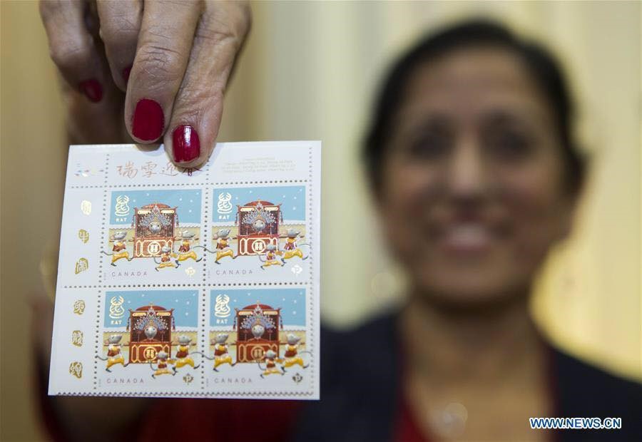 Nhân viên Bưu điện Canada chụp hình cùng mẫu tem nội địa năm Canh Tý tại trung tâm văn hoá Trung Quốc ở Toronto, Canada ngày 16.1.2020. Ảnh: Xinhua