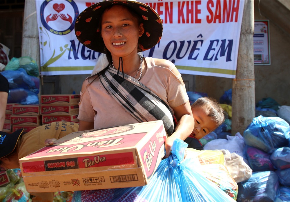Gùi đứa con nhỏ mới mấy tháng tuổi sau lưng, người phụ nữ Vân Kiều nhận món quà gồm 1 két mì tôm, 1 chai dầu ăn, 1 gói bột ngọt, 2 túi áo quần cũ.