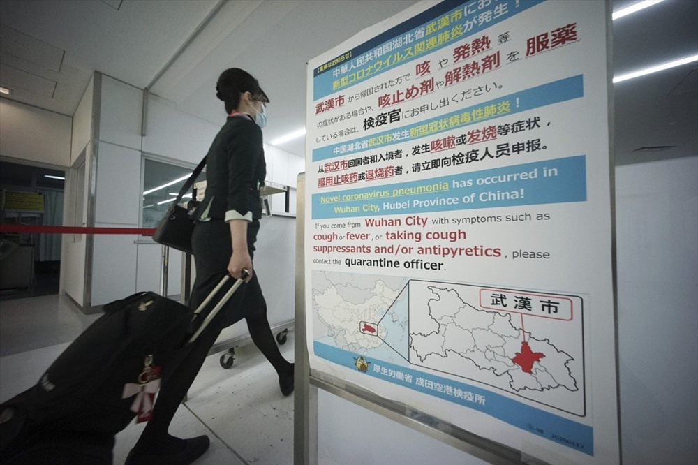 Một tiếp viên hàng không đi ngang qua máy quét nhiệt độ cơ thể và bảng thông báo về coronavirus tại sân bay quốc tế Narita hôm 23.1. Ảnh: AP