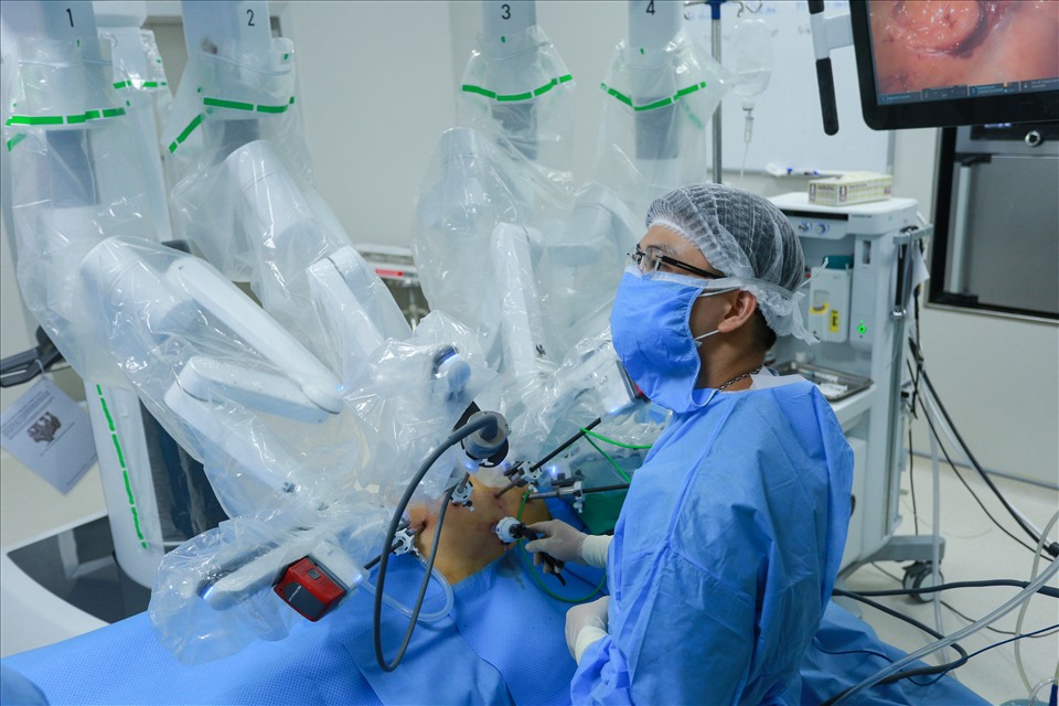 Mổ phụ - thạc sĩ, bác sĩ Trần Đình Tân vừa quan sát màn hình, vừa hỗ trợ tiến sĩ, bác sĩ Phạm Văn Bình điều chỉnh vị trí các cánh tay robot. Robot Da Vinci XI có 4 cánh tay, mỗi cánh đều được bọc nylon vô trùng, được thay ra vệ sinh sau mỗi lần phẫu thuật mang lại sự an toàn tuyệt đối cho bệnh nhân.
