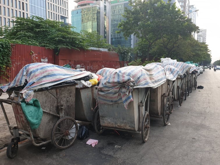 Xe rác nối đuôi nhau nằm dài chờ được chuyển đi trên phố Duy Tân. Công nhân vệ sinh môi trường phải phủ bạt tạm thời lên các xe rác.