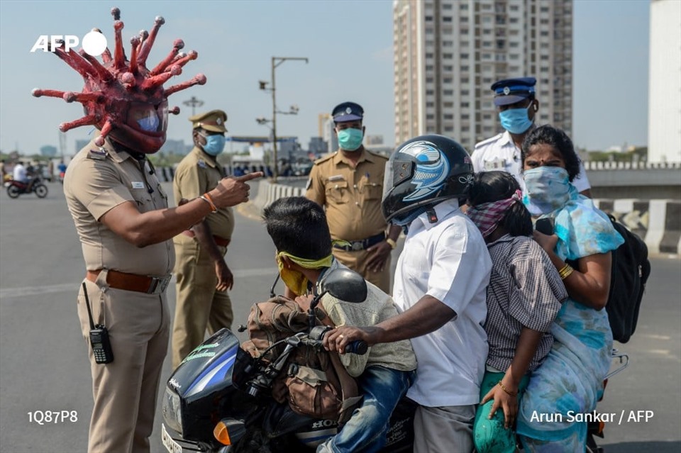 Thanh tra cảnh sát Rajesh Babu đội một chiếc mũ bảo hiểm mô phỏng virus SARS-CoV-2 đang trao đổi với 1 gia đình tại một trạm kiểm soát ở Chennai trong đợt phong tỏa toàn Ấn Độ, ngày 28.3. Ảnh: AFP