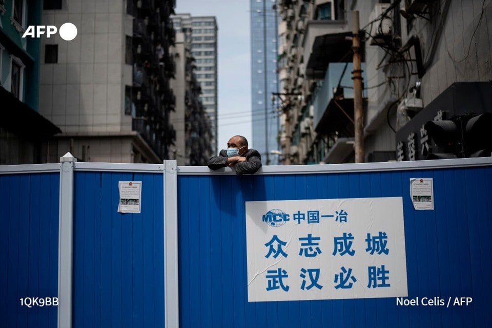 Một người đàn ông đeo khẩu trang đứng đằng sau hàng rào ngăn cách khu dân cư nhằm ngăn chặn lây lan đại dịch COVID-19 ở thành phố Vũ Hán, tỉnh Hồ Bắc, Trung Quốc,  ngày 14.4. Ảnh: AFP
