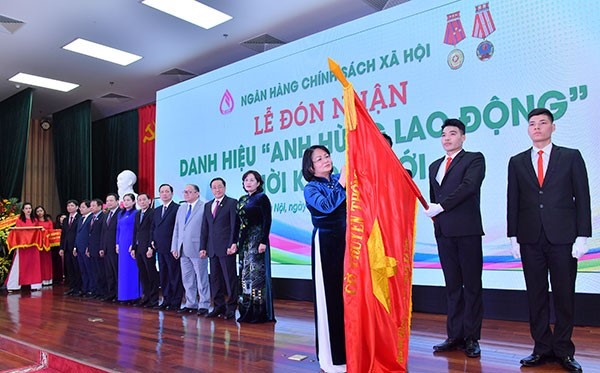 Phó Chủ tịch nước Đặng Thị Ngọc Thịnh đính huy hiệu “Anh hùng lao động” thời kỳ đổi mới lên lá cờ truyền thống của NHCSXH.