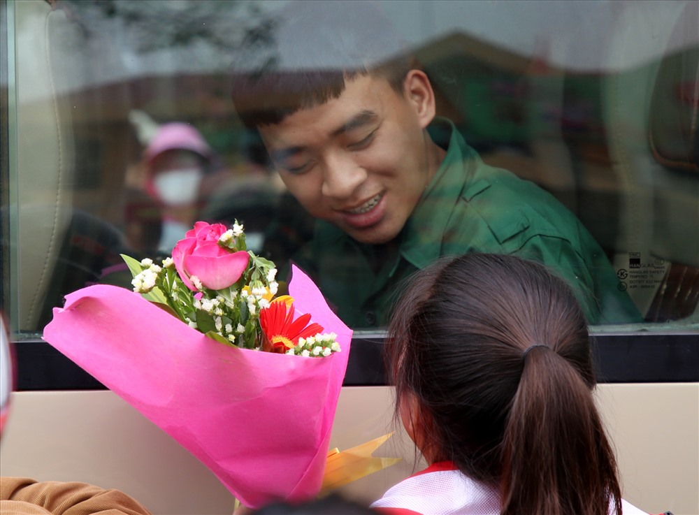 Tân binh cười tươi khi người thân tặng hoa ngoài cửa kính.