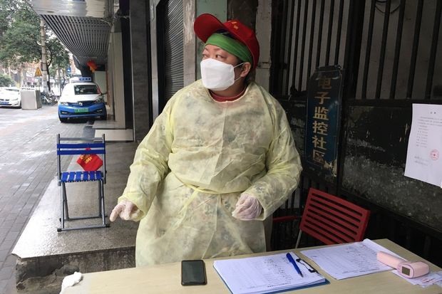 Một người trong tổ dân phố ở Vũ Hán mặc áo mưa, đeo khẩu trang đội mũ làm nhiệm vụ trong ca trực. Ảnh: Wall Street Journal.