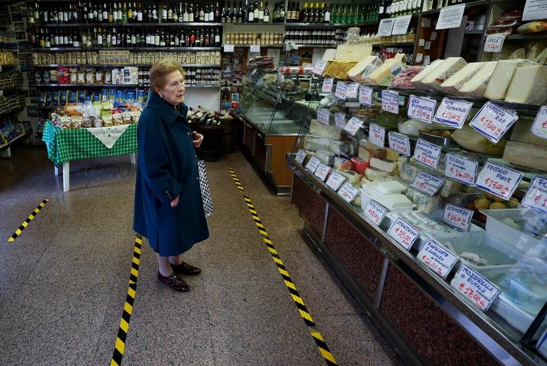 Một phụ nữ đứng chờ sau những vạch vàng đánh dấu khoảng cách tại một cửa hàng tạp hóa ở Rome, Italia. Ảnh: REUTERS/Guglielmo Mangiapane.