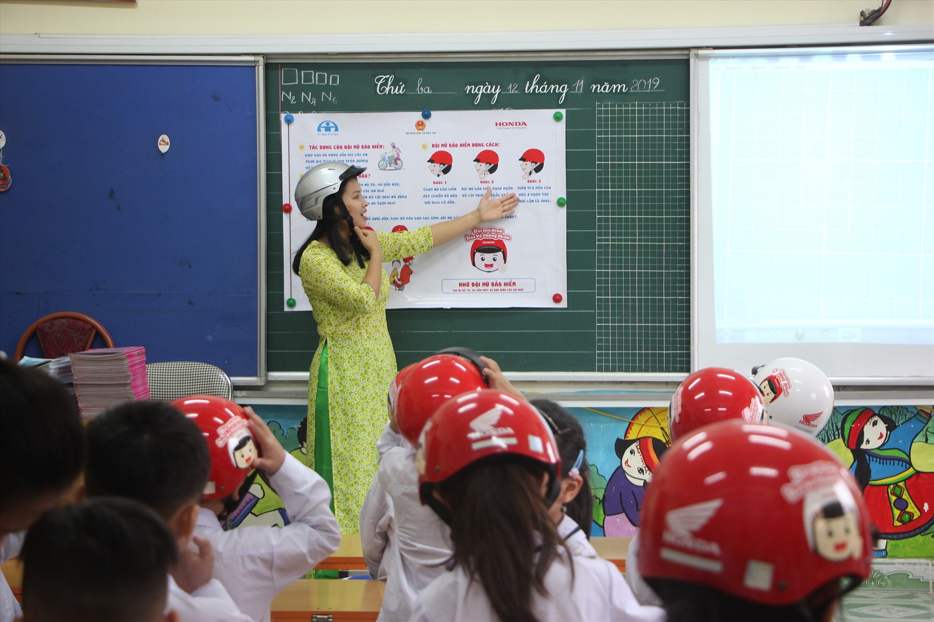 Cô giáo hướng dẫn các em học sinh đội mũ đúng cách.