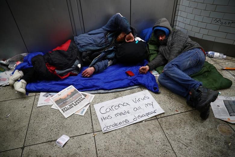 Những người vô gia cư ở London (Anh) nằm bên cạnh biển đề dòng chữ - Dịch COVID-19 khiến những người vô gia cư mất đi nguồn thu nhập.