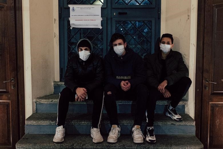 Ba thiếu niên đeo khẩu trang ngồi bên ngoài một tòa nhà công cộng ở San Fiorano, ngày 21.2. Ảnh: Reuters
