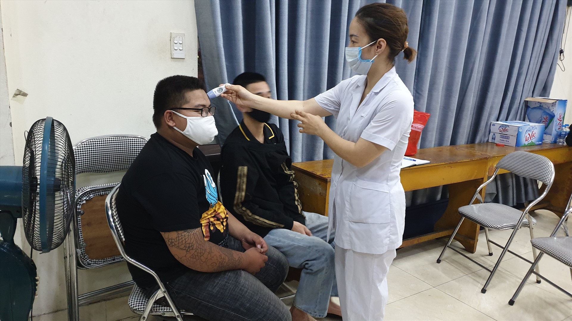 Nhân viên y tế kiểm tra thân nhiệt cho những người bị mời về nhà văn hóa phường do sau 22h vẫn ra đường. Ảnh: Nguyễn Hùng