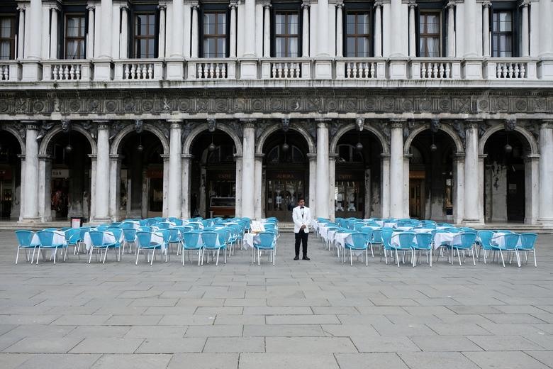 Một người phục vụ đứng cạnh những chiếc bàn trống bên ngoài một nhà hàng tại Quảng trường St Mark, nơi thường có rất nhiều khách du lịch, một ngày sau khi chính phủ Ý thông qua một nghị định với các biện pháp mới khẩn cấp để chứa coronavirus, tại Venice, ngày 5 tháng 3