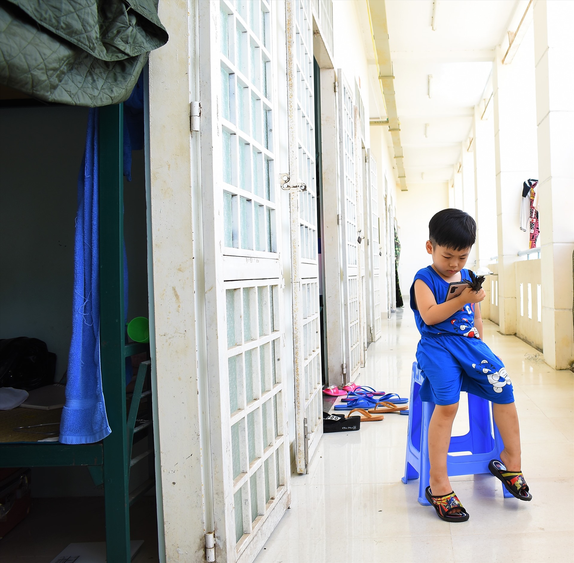 Một bé trai xem điện thoại ngoài hành lang tại một dãy phòng thuộc khu cách ly ở trường quân sự TP.Cần Thơ
