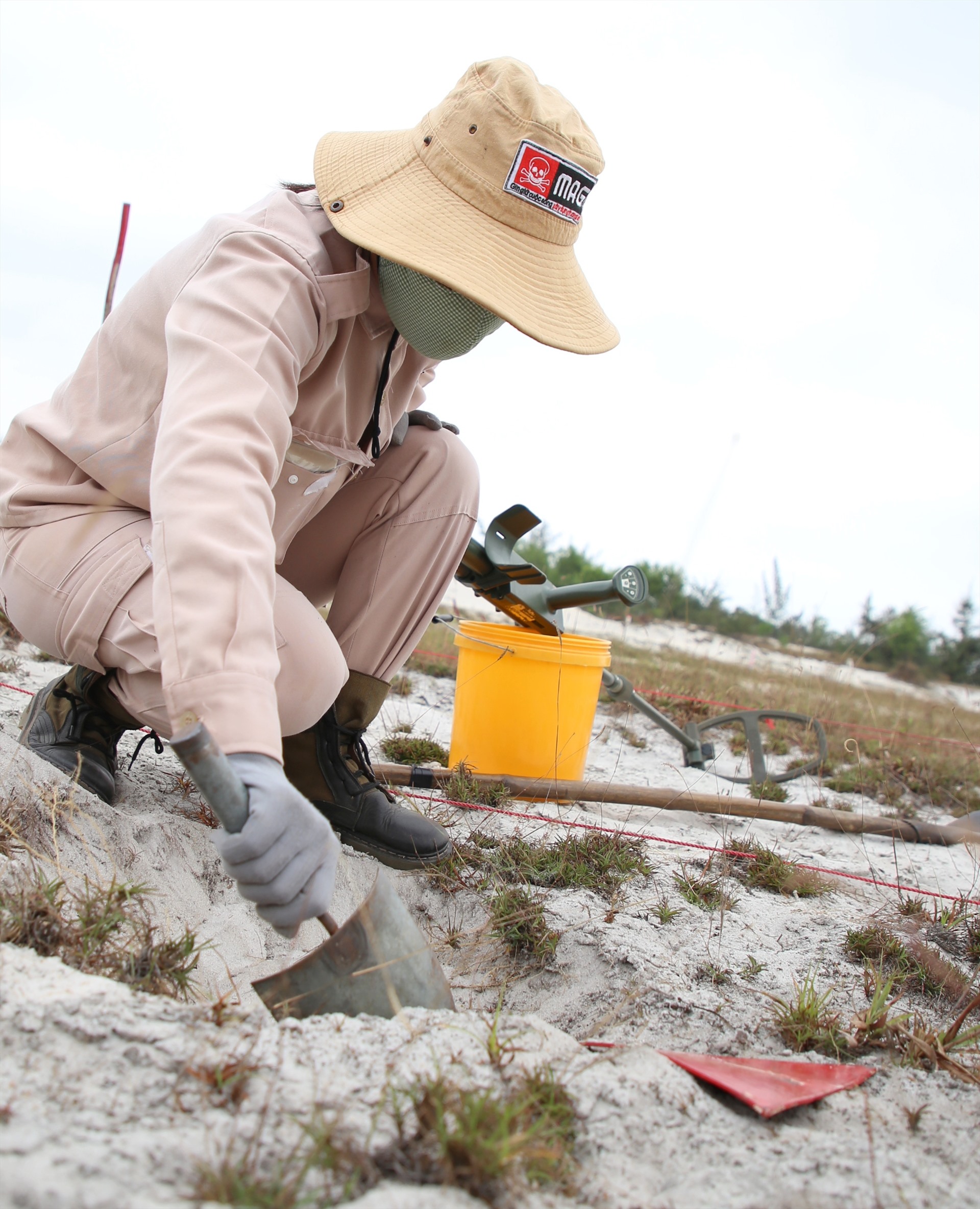 Một thành viên sử dụng chiếc xẻng nhỏ, đào nhẹ từng lớp đất cát ở vị trí có đặt tấm giác màu đỏ để tìm kiếm vật mà máy rà bắt được.