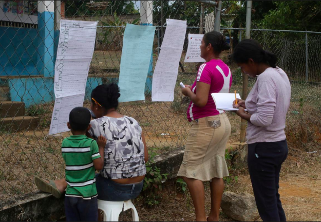 Cha mẹ tới chép bài tập về nhà cho con bên ngoài hàng rào trường học ở El Pao, Venezuela, ngày 1.3. Ảnh: Reuters
