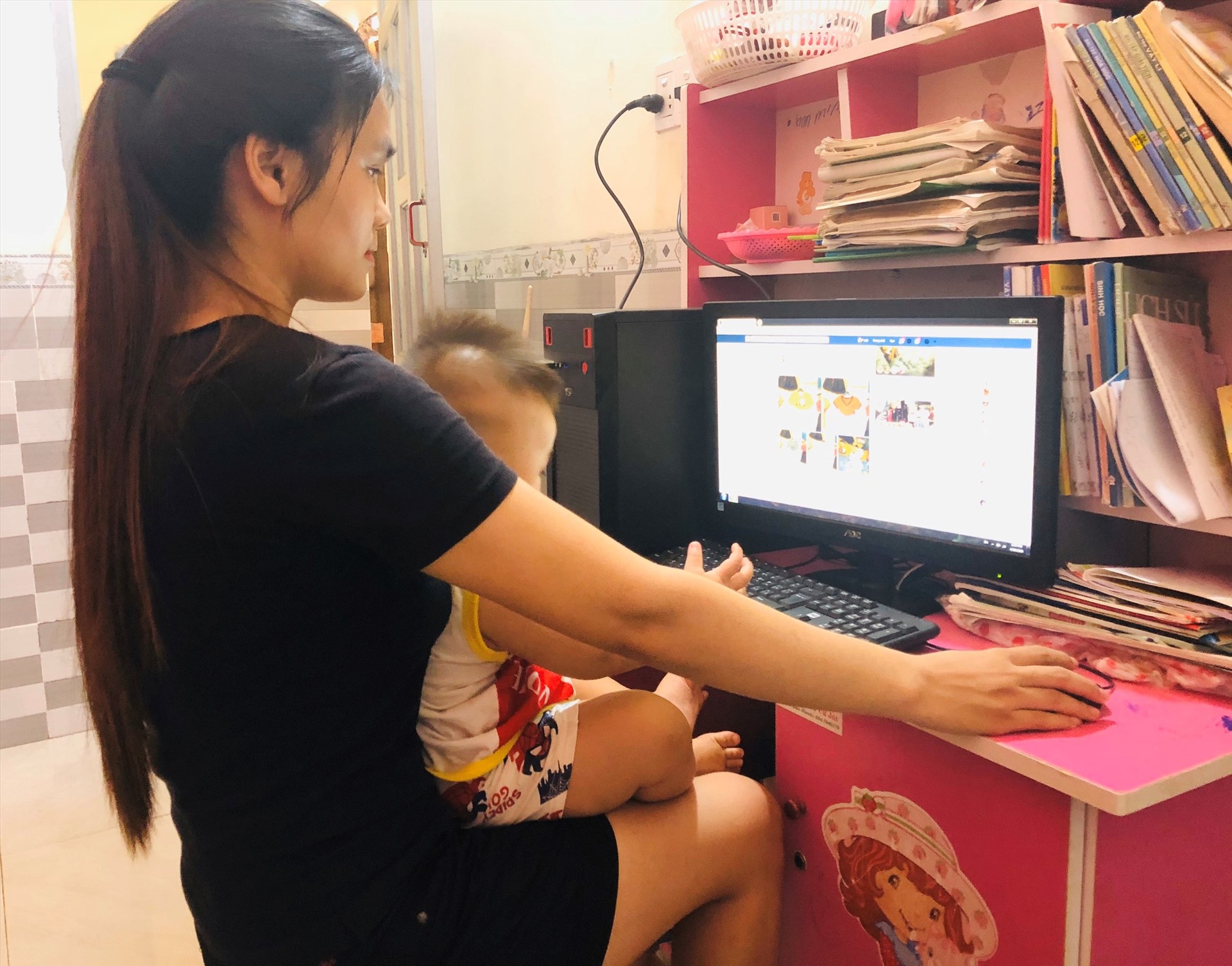 Một giáo viên mầm non ở Đắk Lắk vừa bế con vừa tranh thủ bán hàng online để kiếm thêm thu nhập trong mùa dịch COVID-19. Ảnh: Tú Sương