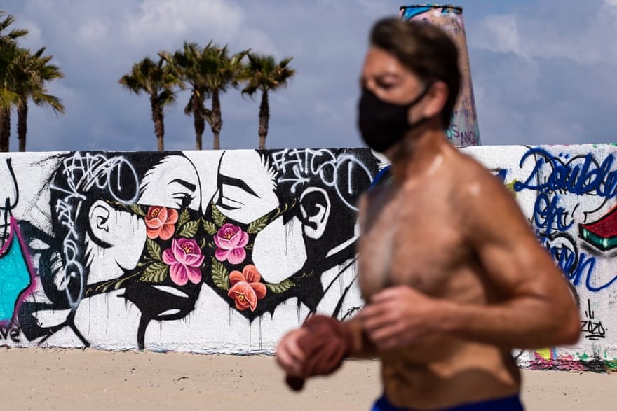Một người đàn ông đeo khẩu trang chạy bộ qua bức tranh tường cặp đôi hôn nhau qua khẩu trang ở Los Angeles, Mỹ. Ảnh: EPA.
