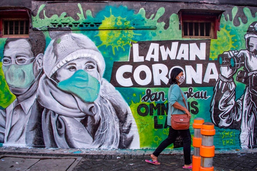 Một người phụ nữ đi ngang qua một bức tranh tường kêu gọi mọi người chiến đấu với COVID-19 ở Surabaya, Đông Java, Indonesia. Ảnh: AFP/Getty Images.