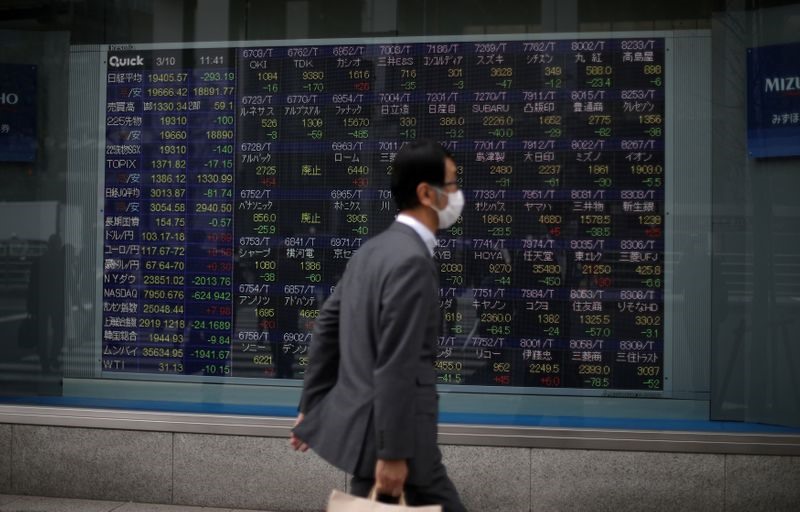 Một người đàn ông đeo khẩu trang trước một bảng báo giá chứng khoán  bên ngoài một công ty môi giới ở Tokyo. Ảnh: Stoyan Nenov/Reuters