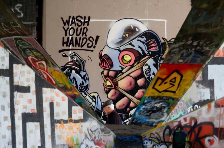 Một người đàn ông đi ngang qua bức vẽ tranh đường phố với dòng chữ “Wash your hand” (Hãy rửa tay) ở Vienna, Áo. Ảnh: Reuters