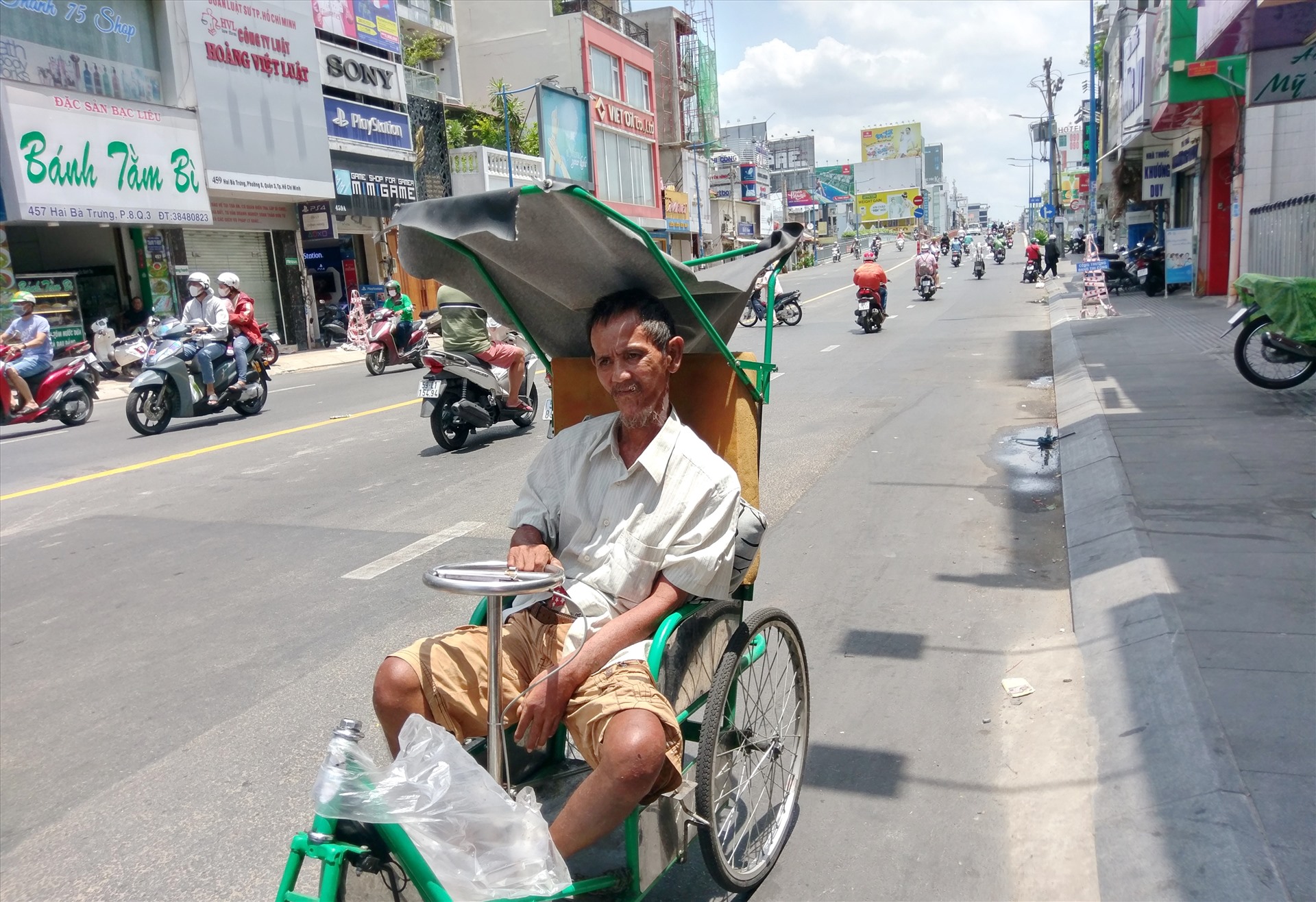 Một cụ ông ngồi xe lăn bán vé số di chuyển dưới lề đường Hai Bà Trưng không một bóng cây trong tiết trời nắng nóng.  Ảnh: Minh Quân