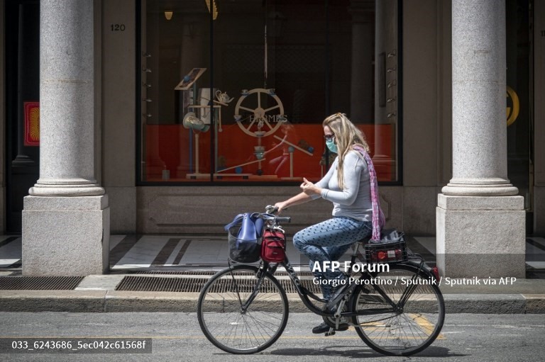 Một phụ nữ đeo khẩu trang đạp xe ở trung tâm đại lộ Via Roma trước một cửa hàng đóng cửa tại Torino, Italia. Ảnh: AFP