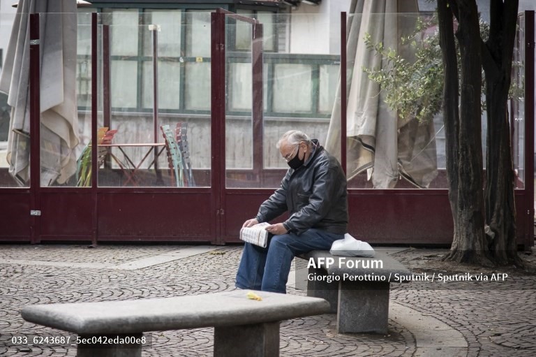 Một người đàn ông đeo khẩu trang ngồi đọc báo gần một quán bar đóng cửa tại Torino, Italia. Ảnh: AFP