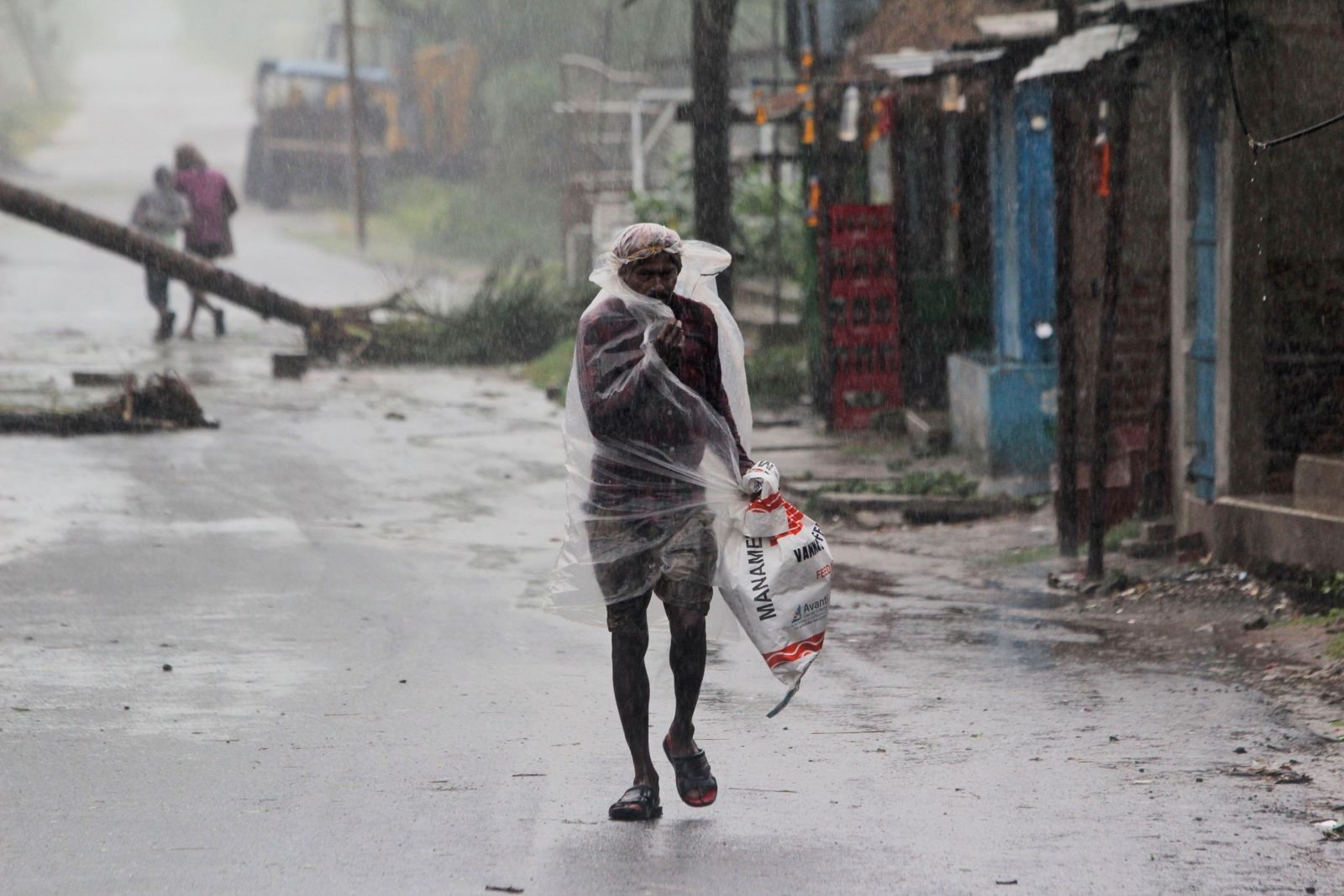 Một người đàn ông lớn tuổi cố gắng che chắn cơn mưa lớn bằng tấm nilon mỏng manh ở Bhadrak, Ấn Độ. Ảnh: AFP