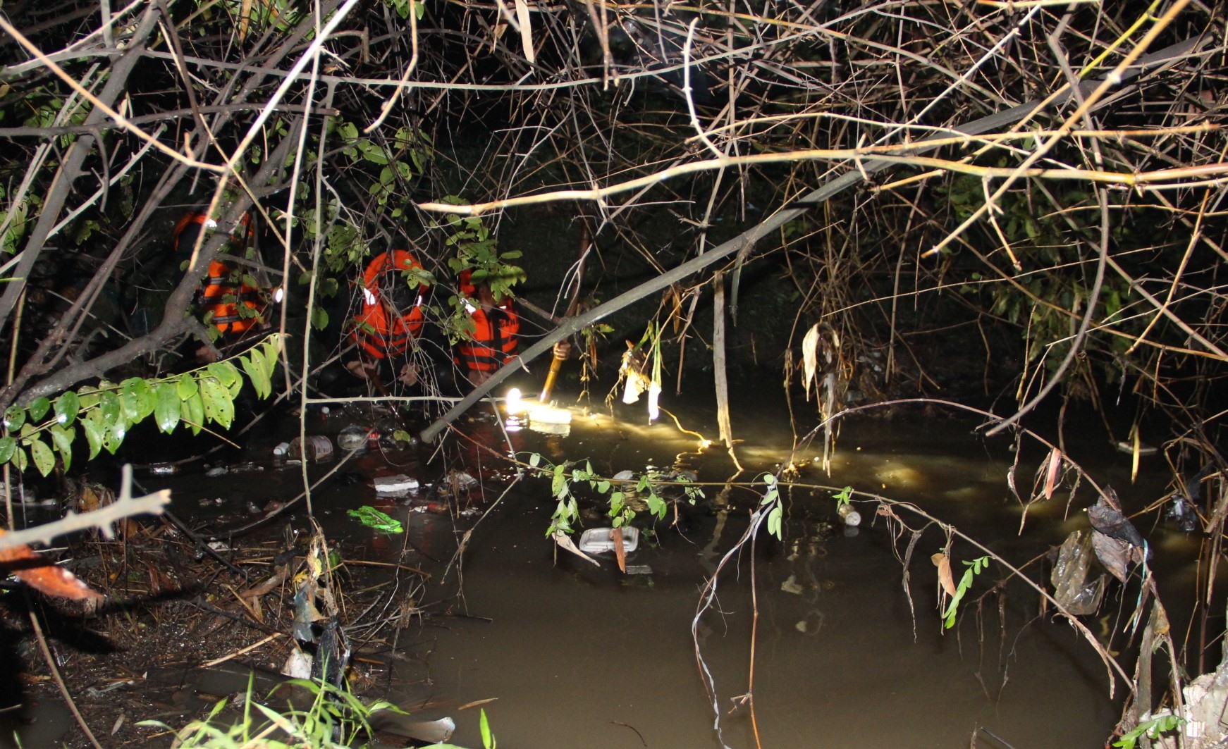 Cảnh sát mò mẫm dưới con suối chảy ra sông Đồng Nai tìm kiếm cháu bé lúc 0h15 ngày 28.5. Ảnh: Đình Trọng