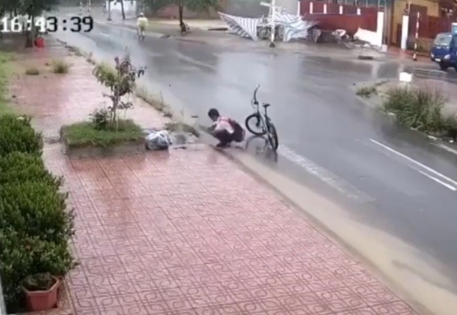 Hình ảnh em Đạt dứng xe đạp, dùng tay không dọn rác bị nghẹt tại cống thoát nước trên đường, được một camera dân cư ghi được- ảnh Chụp màn hình