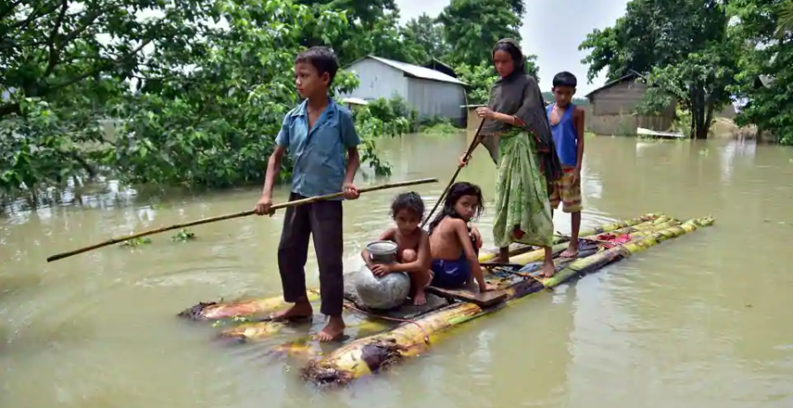 Các trẻ em đang ngồi trên một chiếc bè tự chế để di chuyển qua khu vực lũ lụt ở làng Mayong, huyện Morigaon của bang Assam, Ấn Độ hôm 29.6. Ảnh: Reuters
