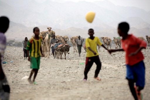 Trẻ con chơi bóng trong khi xa xa, những con lạc đà đang chở muối giúp người dân. Ảnh: AFP